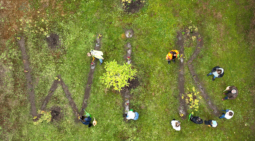 Luftaufnahme von Menschen, die auf einer Wiese die Buchstaben W I R angelegt haben