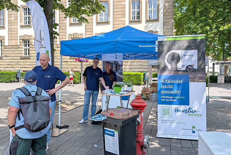 Informationsstand mit blauem Pavillon und Banner zum Thema Altkleider-Abholung auf dem Umweltmarkt im Freien
