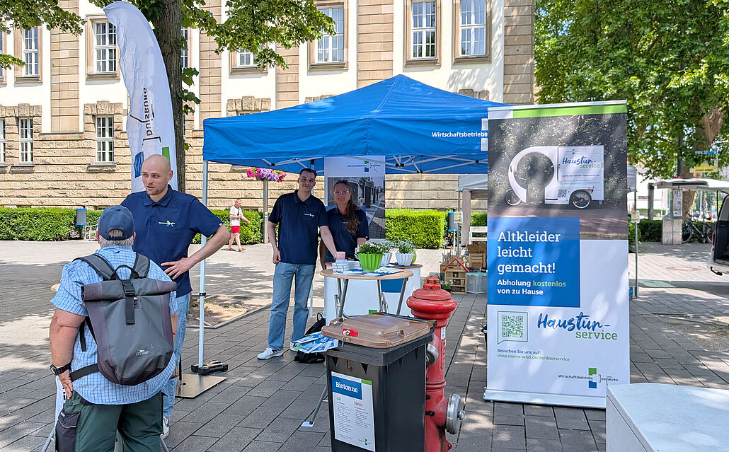 Informationsstand mit blauem Pavillon und Banner zum Thema Altkleider-Abholung auf dem Umweltmarkt im Freien