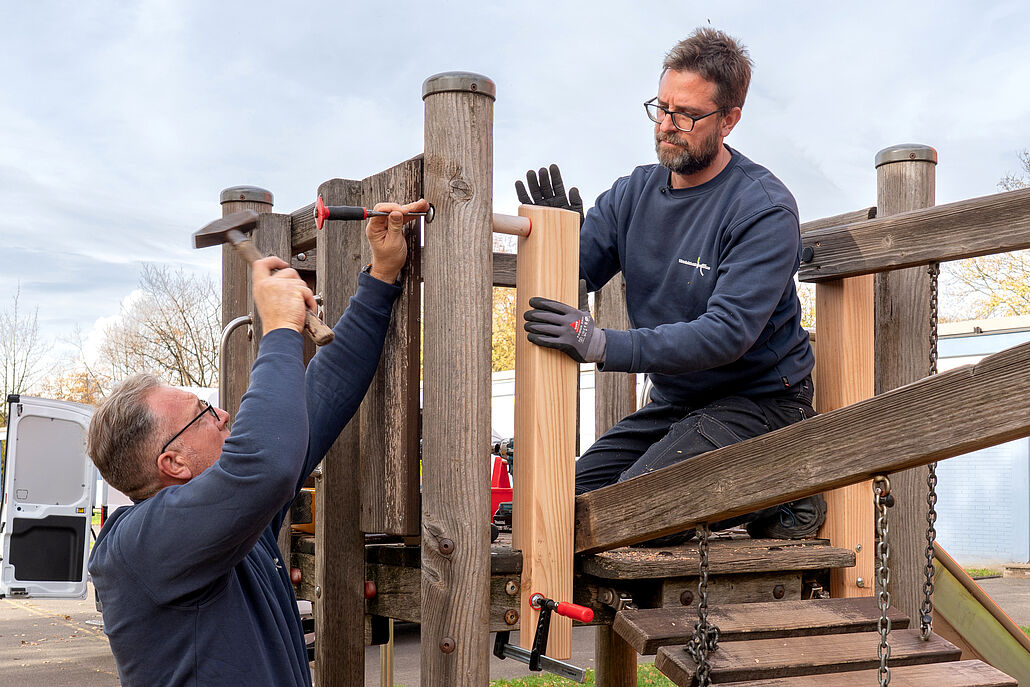 Zwei Männer montieren Holzlatten an einem Spielplatzgerüst aus Holz