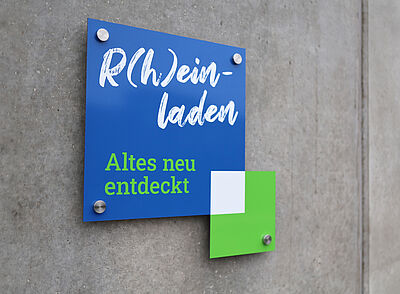 Schild an einer Betonwand mit der Aufschrift 'R(h)ein-laden Altes neu entdeckt'