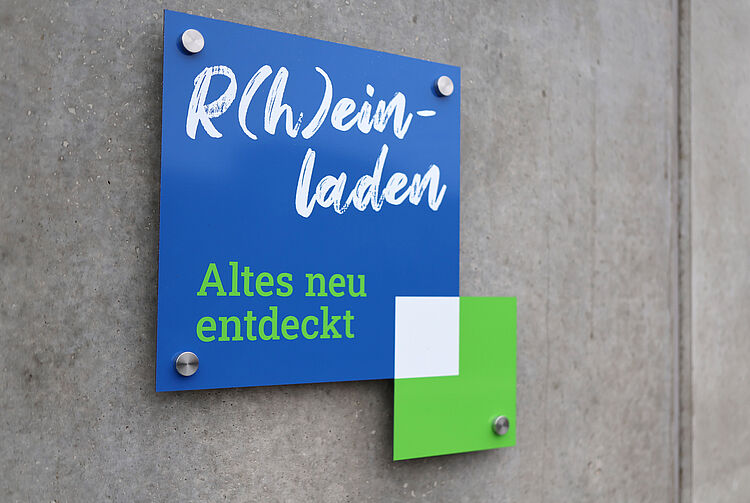 Schild an einer Betonwand mit der Aufschrift 'R(h)ein-laden Altes neu entdeckt'
