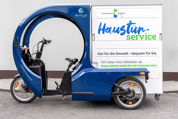 Blaues Lastenfahrrad mit geschlossener Ladebox und Aufschrift 'Haustürservice' für Abholung von Altkleidern