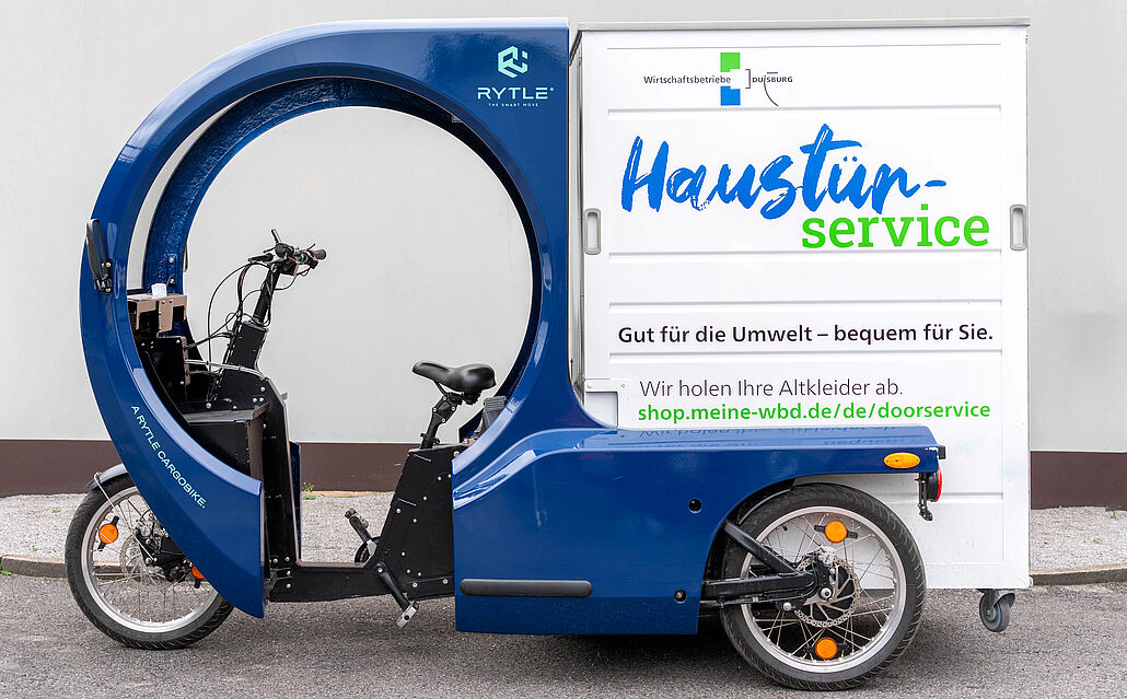 Blaues Lastenfahrrad mit geschlossener Ladebox und Aufschrift 'Haustürservice' für Abholung von Altkleidern