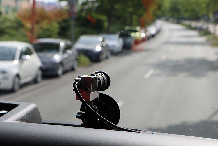 Kleine Kamera auf dem Armaturenbrett eines Fahrzeugs, Straße mit geparkten Autos im Hintergrund