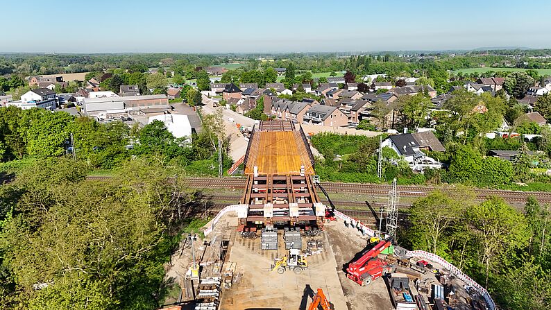 Luftaufnahme einer Baustelle an der Cölve-Brücke mit orangefarbenem Gerüst und mehreren Baugeräten, umgeben von Bäumen und Wohnhäusern.