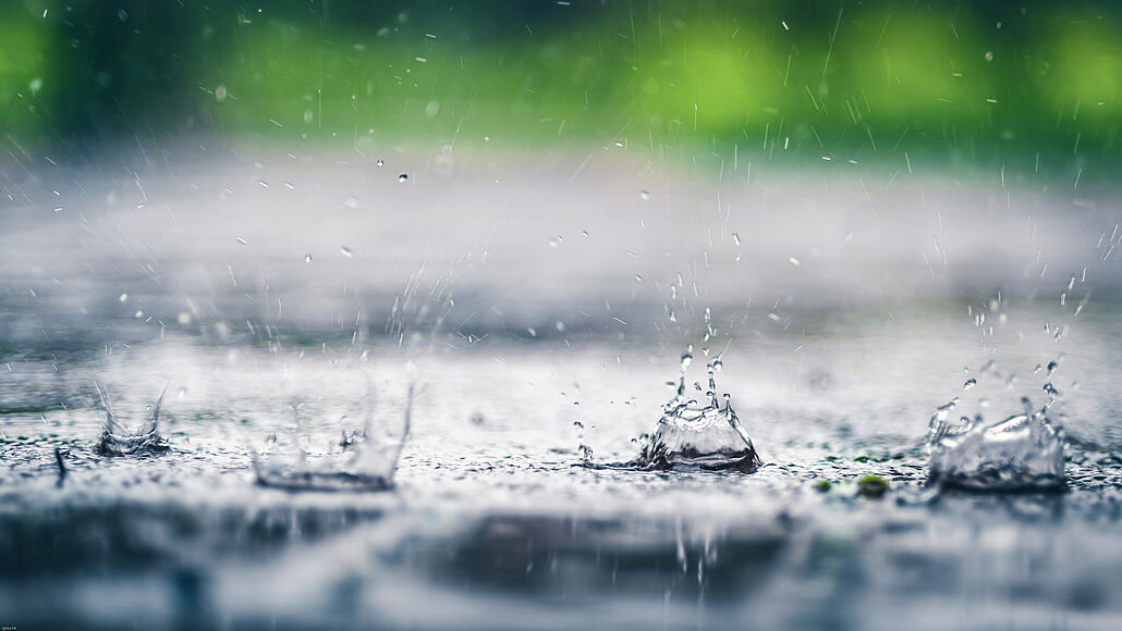 Regentropfen fallen auf eine Wasseroberfläche und erzeugen Spritzer