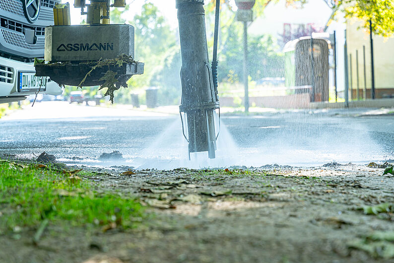 Nahaufnahme der Sinkkastenreinigung, ein Schlauch sprüht mit Hochdruck Wasser auf den Boden