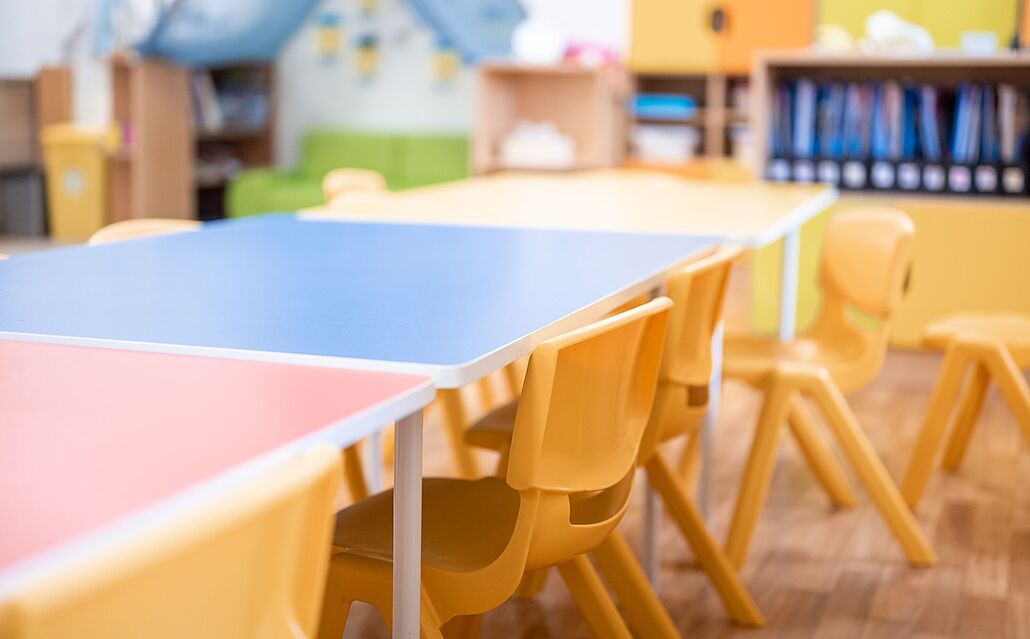 Leere Kindertischgruppe mit bunten Tischen und gelben Stühlen in einem Kindergartenraum