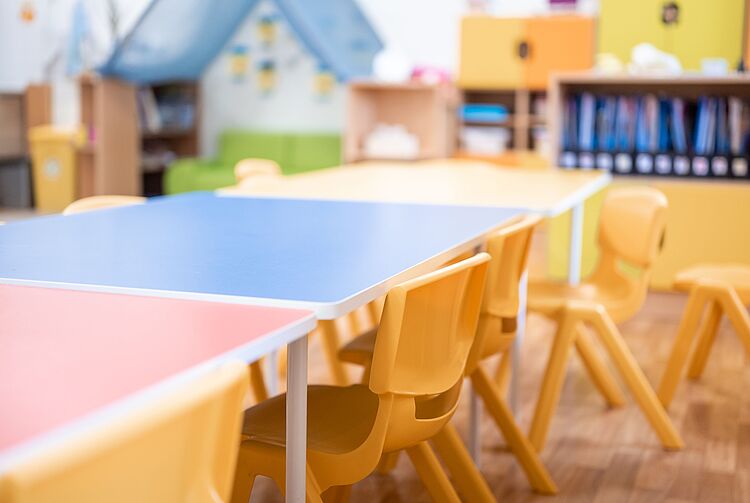 Leere Kindertischgruppe mit bunten Tischen und gelben Stühlen in einem Kindergartenraum
