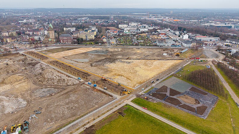 Luftaufnahme des großen Baugeländes des IGA-Eingangsbereichs mit mehreren Baumaschinen und angrenzenden Grünflächen in einer Stadtumgebung