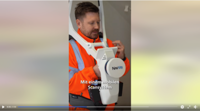 Person in orangefarbener Arbeitskleidung hält ein mobiles Scansystem mit der Aufschrift 'NavVis'