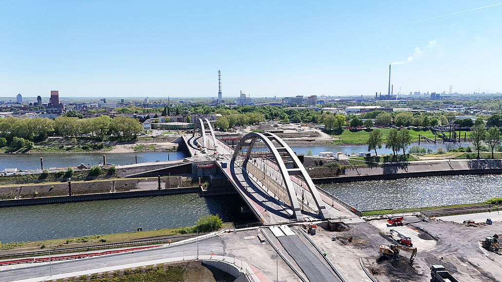 Luftaufnahme der OB-Karl-Lehr-Brücke mit zwei großen Stahlbögen über einen Fluss und einer Baustelle im Vordergrund
