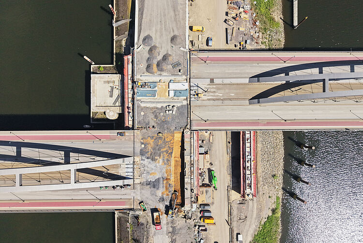 Luftaufnahme der Baustelle an der OB-Karl-Lehr-Brücke über einem Fluss mit Baumaschinen und Baustellenmaterialien auf der Fahrbahn und am Ufer