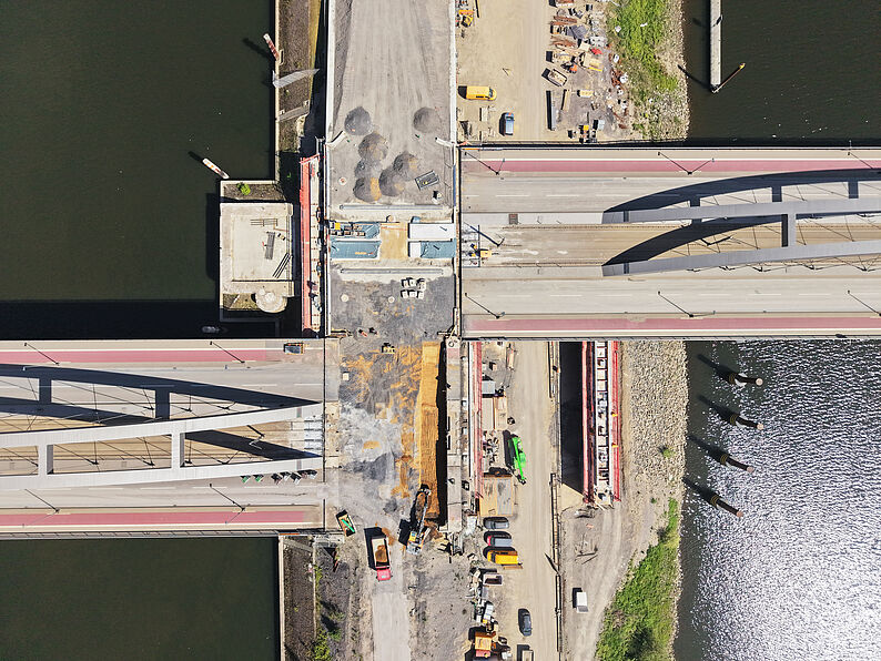 Luftaufnahme der Baustelle an der OB-Karl-Lehr-Brücke über einem Fluss mit Baumaschinen und Baustellenmaterialien auf der Fahrbahn und am Ufer