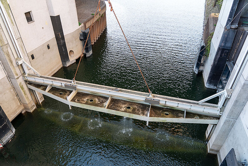 Blick von oben auf eine Wasseranlage mit einem schräg hängenden Metallträger über einem Wasserbecken, aus dem mehrere Wasserstrahlen nach unten spritzen