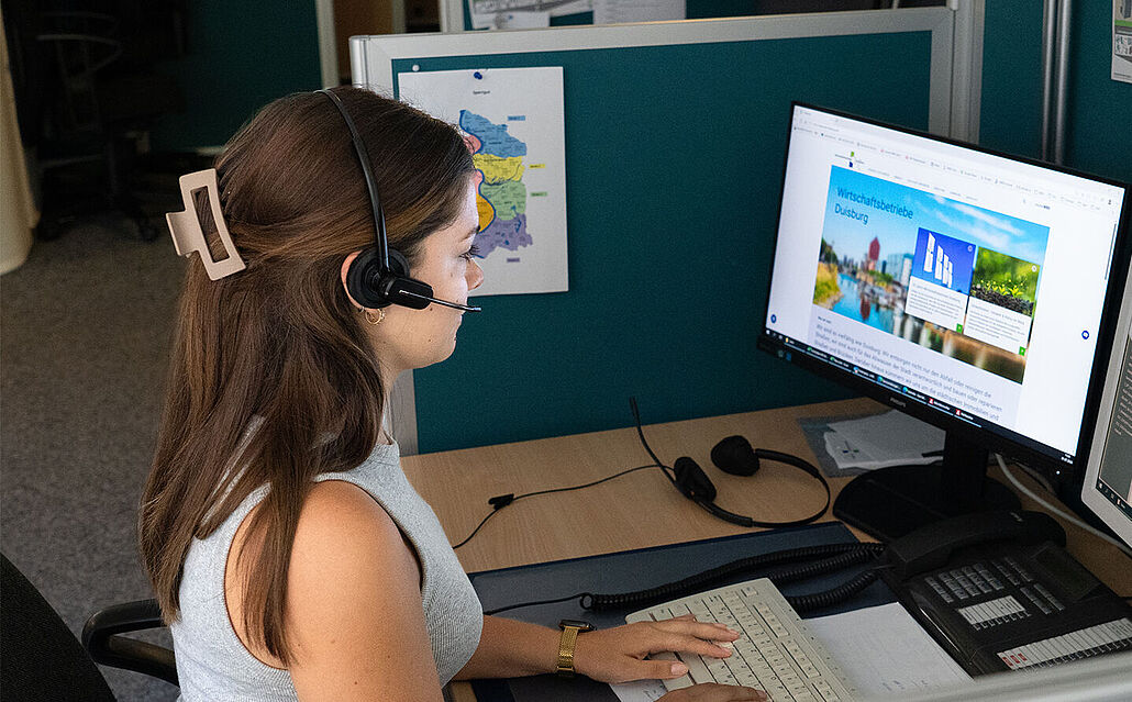 Mitarbeiterin mit Headset sitzt am Schreibtisch im Kundencenter der WBD und arbeitet an zwei Monitoren mit Tastatur