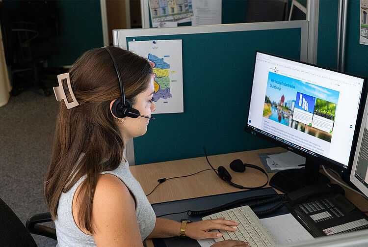 Mitarbeiterin mit Headset sitzt am Schreibtisch im Kundencenter der WBD und arbeitet an zwei Monitoren mit Tastatur