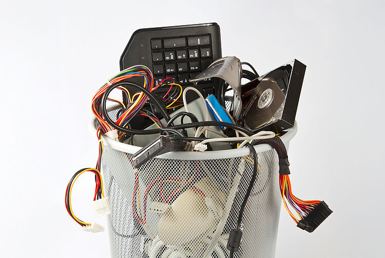 Metallkorb mit verschiedenen Elektroschrottteilen wie Tastatur, Kabeln, CD und Computerbauteilen