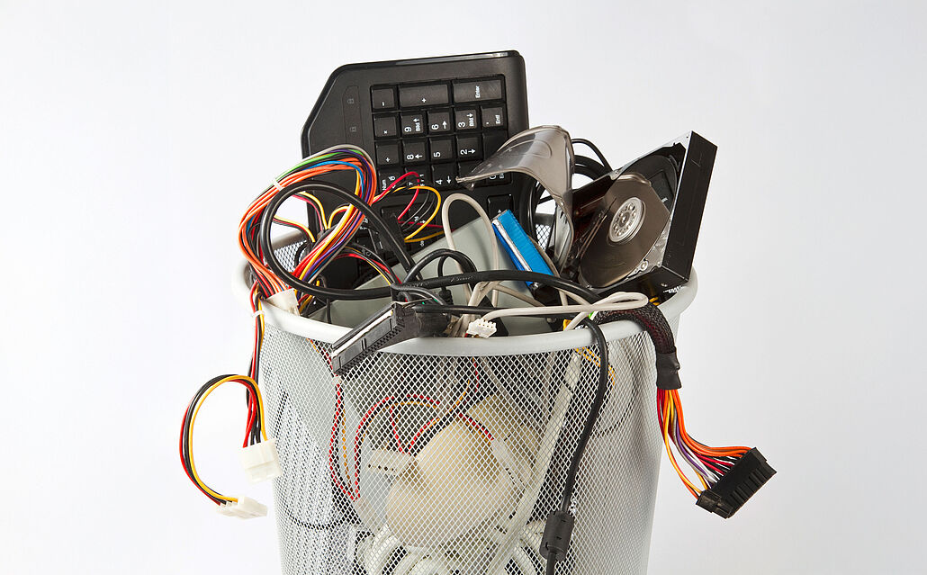 Metallkorb mit verschiedenen Elektroschrottteilen wie Tastatur, Kabeln, CD und Computerbauteilen